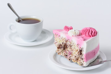 A slice of cake with white and pink cream on a saucer on a white background with a mug of tea