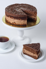 Chocolate cake on the cake table with a mug of tea and a cut piece on a saucer on a white background