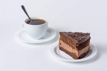A slice of chocolate cake with a cup of tea on a white background