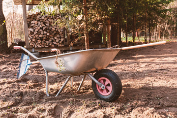 A wheelbarrow holding a rake in front of a pile of wood
