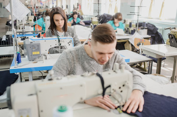 Obraz premium close up photo of a young man and other seamstresses sewing with sewing machine in a factory