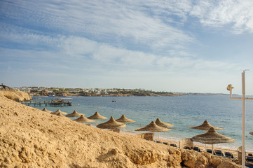 Thatched beach umbrellas and loungers on a beach at an idyllic tropical resort for a summer vacation