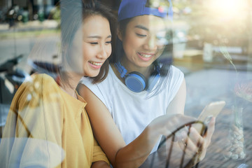 Two positive Vietnamese teenage girls resting pointing at screen of smartphone and exploring new...