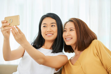Pretty smiling Asian teenage girls taking selfie on smartphone