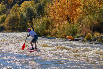 Sportsman paddling on rapids in whitewater river on a inflatable stand up paddle board (SUP)