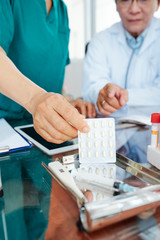 Close-up image of doctor pointing at blister with pills in hands of nurse