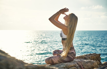 Fototapeta na wymiar Young blonde woman doing yoga on the cliff by the sea at sunrise 