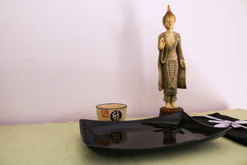 Statuetta di un buddha con un piatto quadrato e tovagliolo neri con tazzina stile orientale appoggiati su una tovaglietta verde