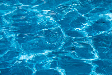 Blue and bright ripple water surface in swimming pool with sun reflection.