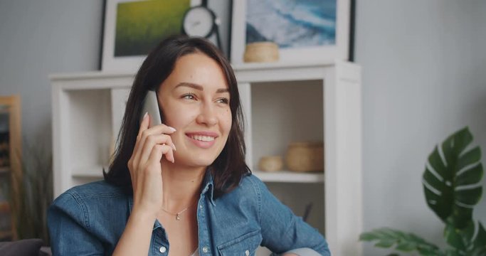 Happy young lady student is talking on mobile phone holding smartphone in apartment. Modern communication, cheerful millennials and leisure time concept.