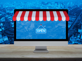 Desktop modern computer monitor with online shopping store graphic and open sign on wooden table over city tower, street, expressway and skyscraper, Business internet shop online concept