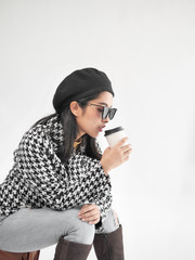 Portrait of Asian woman wearing winter jacket and sitting on vintage brown bag, and drinking coffee cup.