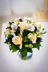 delicate beautiful bouquet with coral roses and blue berries is on the table