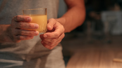 Healthy dinner. Cropped shot of man standing in kitchen with glass of fresh organic orange juice. Dark blur background.