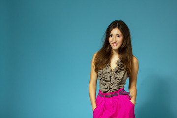 Fototapeta premium Beautiful cheerful teen girl, isolated over blue background. Young pretty woman posing at studio, copy space