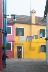 Fototapeta na wymiar Colorful houses on the Italian island Burano, province of Venice, Italy. Multicolored buildings in fog, Italian courtyard with dry laundry outdoor.