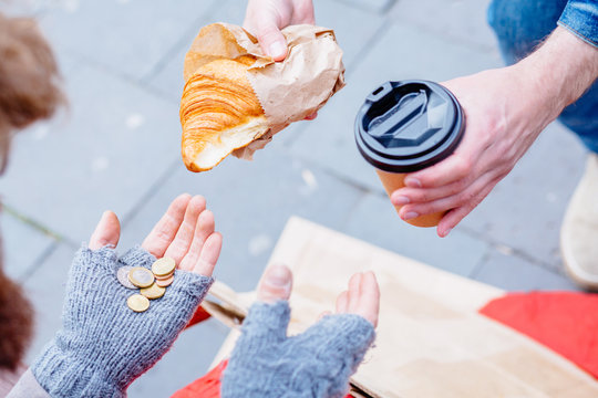 Croissant From Stranger. Share Food With Hungry Unhappy Lonely Man. Close Up Of Unidentified Man's Hands Giving Homeless Beggar Some Hot Drink And Food Bread Outdoors. Concept Of Helping Poor People