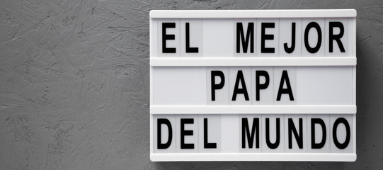'El Mejor Papa Del Mundo' words on a modern board over gray surface. Overhead, from above, flat lay. Father's day. Copy space.