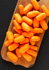 Peeled baby carrots on a rustic wooden board over black background, top view. Overhead, from above, flat lay. Close-up.
