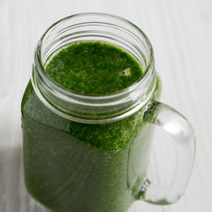 Green smoothie with avocado, spinach and banana in a glass jar mug over white wooden background, low angle view. Close-up.