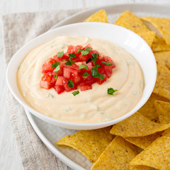 Homemade cheesy dip in a bowl, yellow tortilla chips, side view. Close-up.
