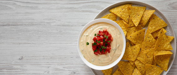 Homemade cheesy dip in a bowl, yellow tortilla chips, overhead view. Top view, from above, flat...