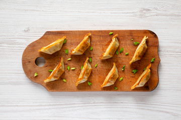 Homemade gyoza on a rustic wooden board over white wooden surface, top view. Flat lay, overhead, from above. Closeup.