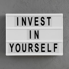 'Invest in yourself' words on a light box on a concrete surface, overhead view. Flat lay, from above, top view.