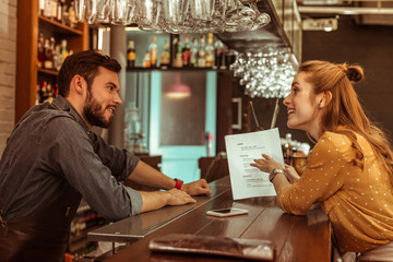 Bewitching woman discussing a menu with handsome dark-haired bearded bartender