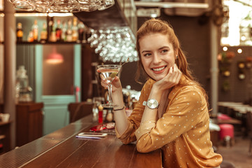 Smiling woman holding martini drink sitting at the bar counter