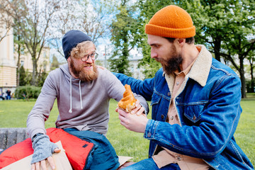 Sympathetic beard hipster man giving his breakfast- coffee and croissant while helpless hungry...