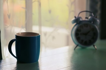 Coffee cup and blur vintage alarm clock closeup table in morning