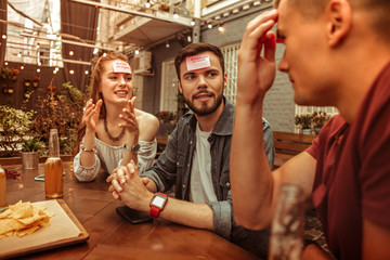 Happy group of friends playing hedbanz game at the bar.