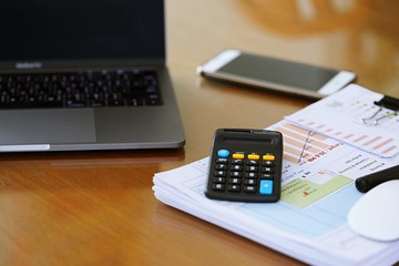 Laptop, smartphone, calculator and pile of paper on desk closeup