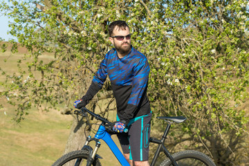 Fototapeta premium Cyclist in shorts and jersey on a modern carbon hardtail bike with an air suspension fork rides off-road on green hills near the forest 