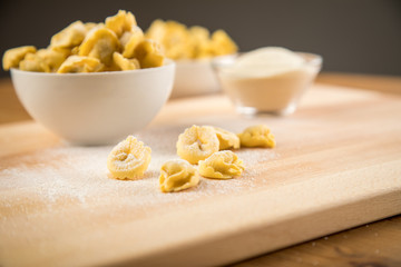 Frische, rohe Cappelletti Tortellini Pasta mit Mehl und Grieß in Porzellan Schale auf Holz Brett