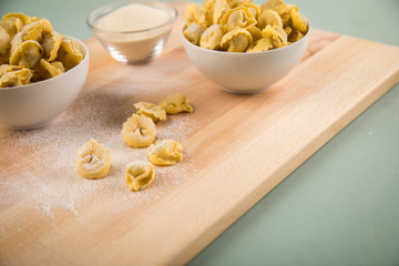 Frische, rohe Cappelletti Tortellini Pasta mit Mehl und Grieß in Porzellan Schale auf Holz Brett und Pastell Grün Hintergrund