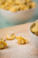 Frische, rohe Cappelletti Tortellini Pasta mit Mehl und Grieß in Porzellan Schale auf Holz Brett und Pastell Grün Hintergrund