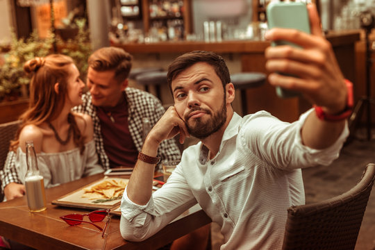 Upset man selfies while his friends hugging at the background.