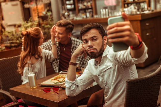 Upset male taking selfies while his mates cuddling at background