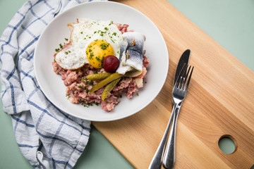 Norddeutscher Hamburger Labskaus mit Rindfleisch Corned Beef, Rote Beete, Kartoffeln, Saure Gurken, Spiegelei und Rollmops auf Teller