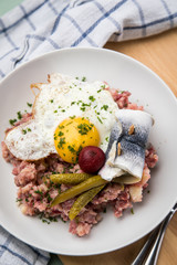 Norddeutscher Hamburger Labskaus mit Rindfleisch Corned Beef, Rote Beete, Kartoffeln, Saure Gurken, Spiegelei und Rollmops auf Teller