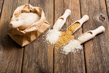 different types of rice on scoops and paper bag, old wood table
