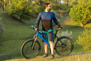 Naklejka premium Cyclist in shorts and jersey on a modern carbon hardtail bike with an air suspension fork rides off-road on green hills near the forest 
