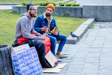 Homeless beggar with young beard handsome man listening to his story while sitting together on the...