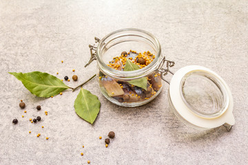 Slices of herring with spices in a glass jar.