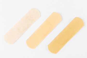 Adhesive plasters of various skin tones from light beige to saturated. A set of adhesive plasters on a white background. Necessary items for summer activities, treatment of wounds, scratches.