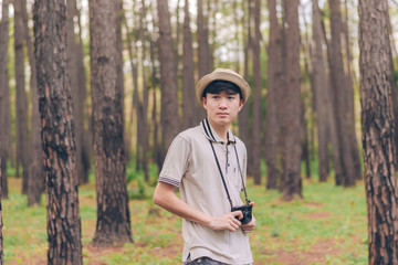 Asia man wears shirt, hat, and camouflage pants are walking and taking photos at the forest.