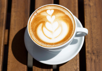Hot cappuccino with froth and pattern on wooden background, top view