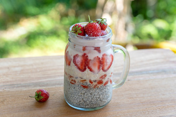 Almond milk chia pudding with fresh red strawberries, goji berries and oat flakes in a glass jar mug. Vegan raw breakfast. Chia seeds and fresh cut fruits and berries dessert